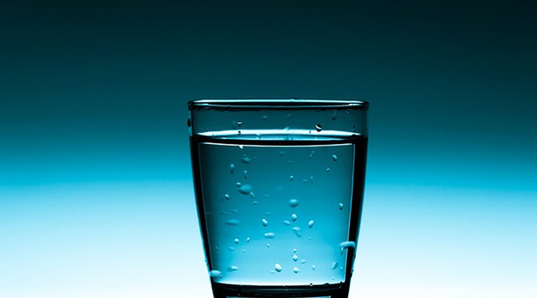 Glass of water with bubbles, blue background.