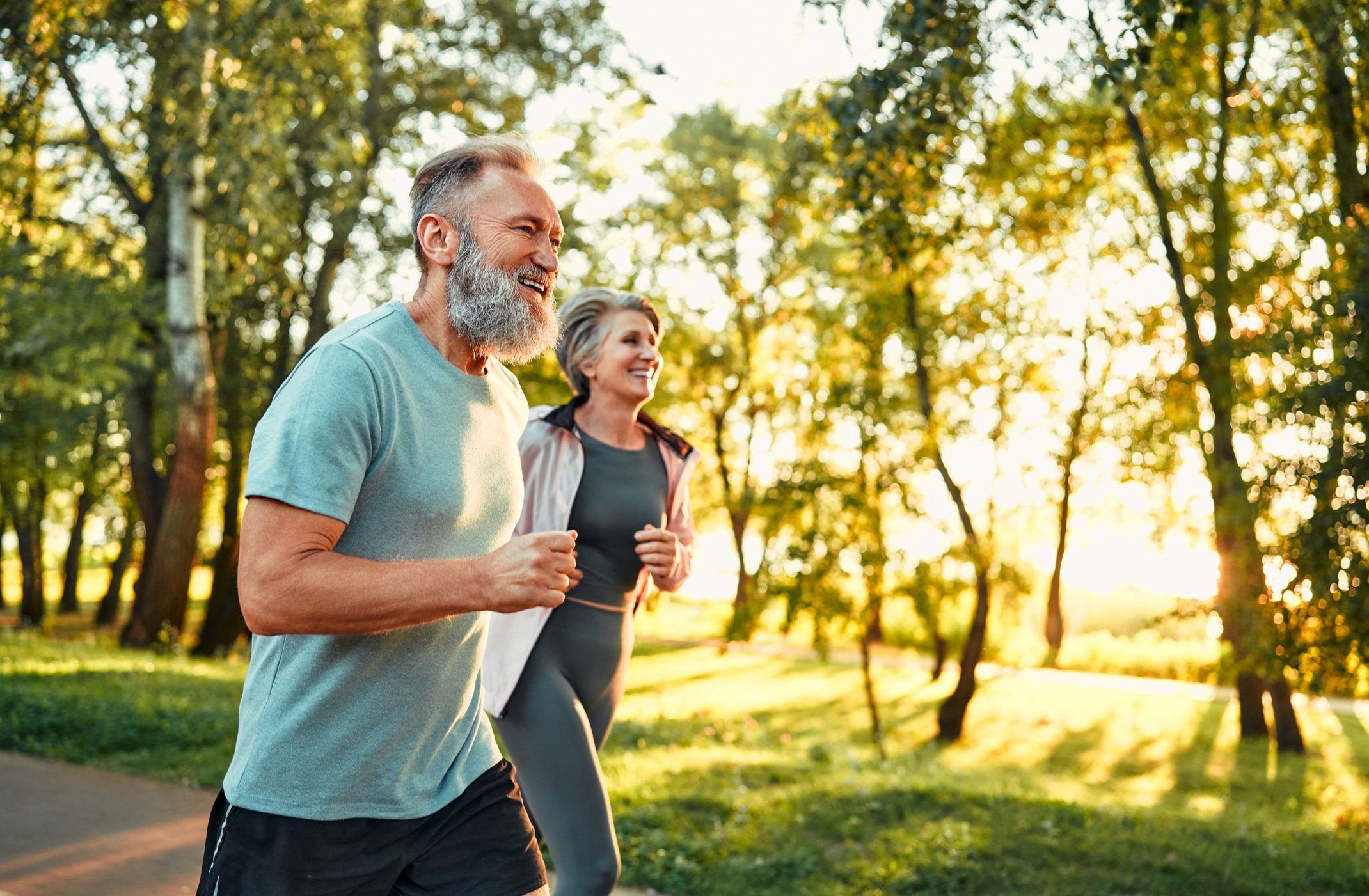 Older couple jogging in a sunny park.