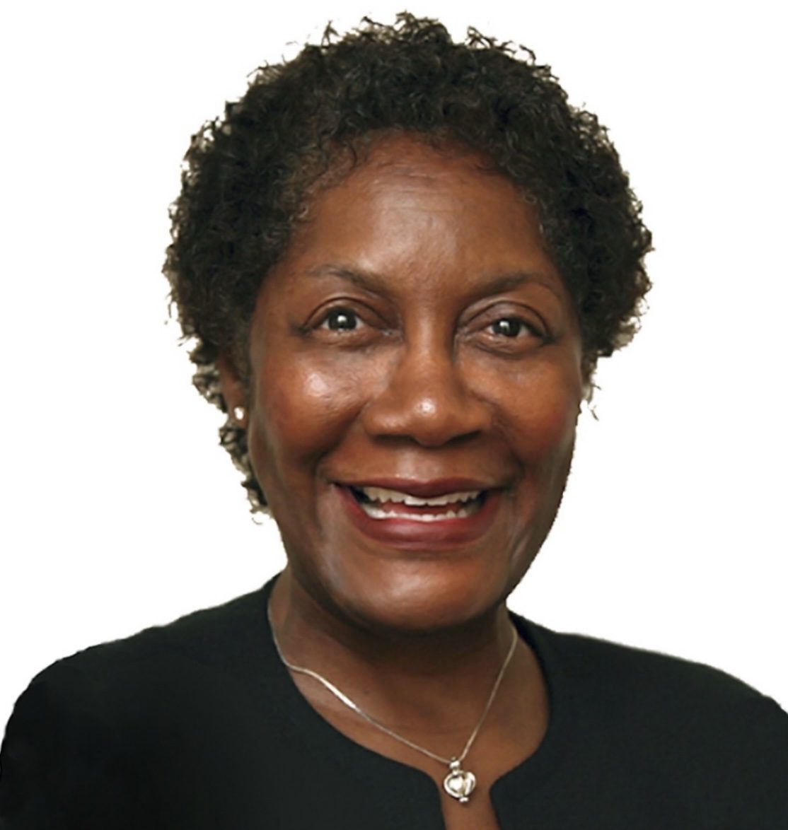 Smiling woman with curly hair wearing a black top and pendant necklace.
