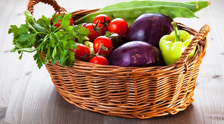 Basket of fresh vegetables on wooden table.