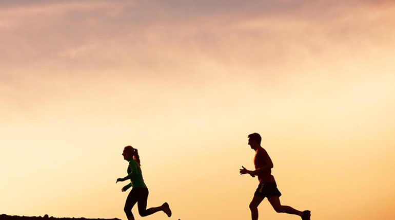 Silhouettes of two people running at sunset.