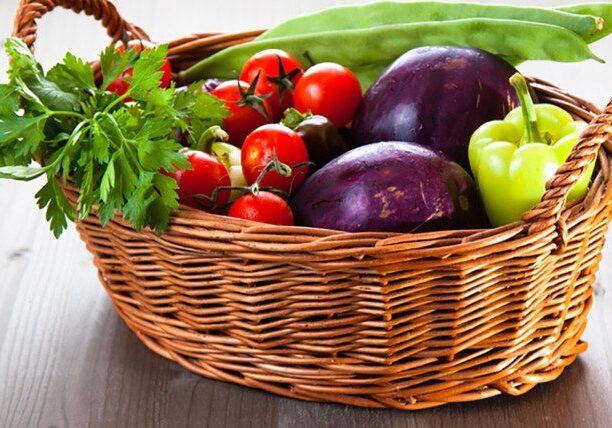 Basket of fresh vegetables on wooden table.
