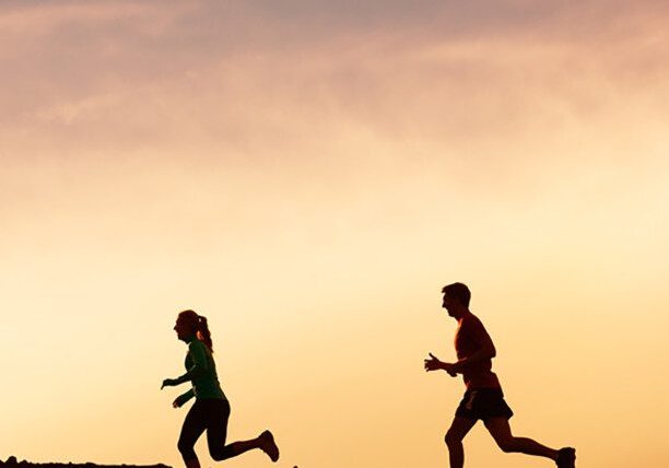 Silhouettes of two people running at sunset.